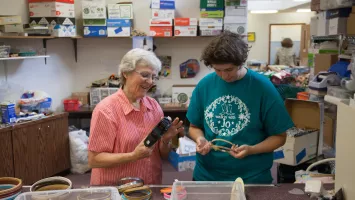 Two women volunteering with MCC Thrift, working with embroidery hoops.