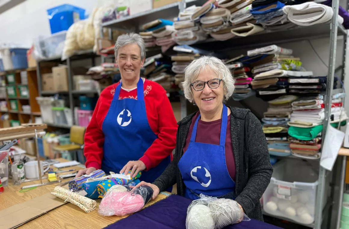 Two volunteers standing close together in front of Fabric on shelves